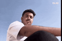 a man is sitting in front of a blue sky with the time 13:22