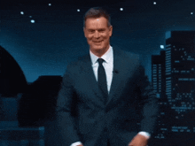 a man in a suit and tie stands in front of a city at night