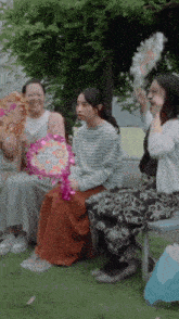 a group of women are sitting on a bench holding fans and one of them is holding a fan that says i love you