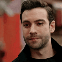 a man with a beard wearing a black shirt and a black jacket