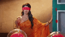 a woman in an orange saree with red blindfolds is standing in front of a green door .