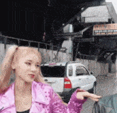 a woman in a pink jacket is standing in front of a white car .