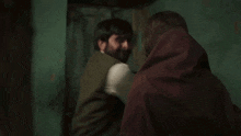 a man and a woman are standing next to each other in a dark room . the woman is wearing a head scarf .