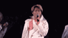 a woman singing into a microphone in a white coat