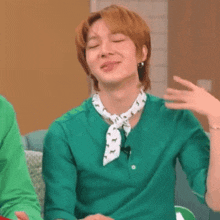 a man in a green shirt and white scarf is sitting on a couch with his eyes closed .