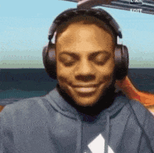 a man wearing headphones and a hoodie is smiling and looking at the camera .