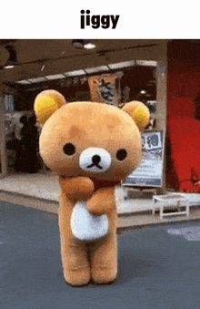 a teddy bear is standing in front of a building with the word jiggy above it