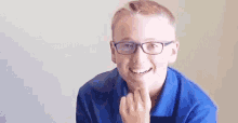 the boy is wearing glasses and a blue shirt and smiling .