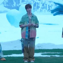 a man in a tie dye shirt is standing in a field with a blue background