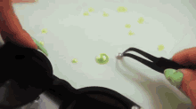 a person with green nails is holding a pair of tweezers over a green bead .