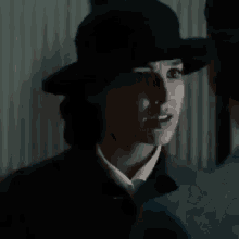 a woman wearing a hat and a suit is standing in the dark .