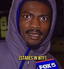 a man in a hooded jacket is holding a fox 5 microphone and says [ stares in wtf ]