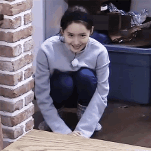 a woman is squatting on the floor next to a brick wall and smiling .