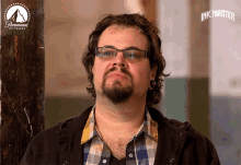 a man wearing glasses and a plaid shirt is standing in front of a paramount network sign