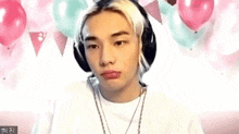 a young man wearing headphones is sitting in front of balloons and making a funny face .