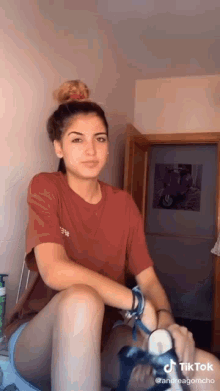 a woman in a red t-shirt is sitting on a bed in a room .