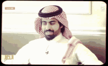 a man wearing a head scarf and a white shirt stands in front of a clock that says 12:33 am