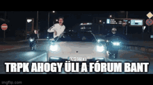 a man driving a car with the words trpk ahogy uli a forum bant