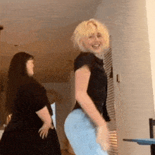 two women are dancing together in a room and one of them is wearing a black shirt and blue jeans .