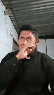 a man is covering his mouth with his hand while wearing a black sweater
