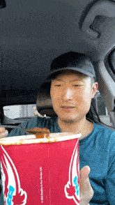 a man is sitting in a car eating a chicken bucket from wendy 's