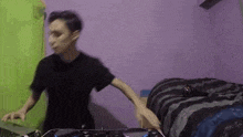 a man in a black shirt is playing music on a dj controller in a bedroom .