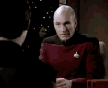 a bald man in a star trek uniform is sitting at a desk