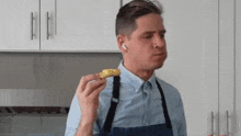 a man wearing an apron is eating a piece of food in a kitchen .