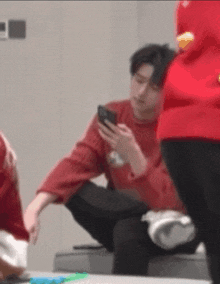 a man in a red sweater is looking at his cell phone