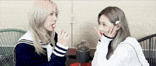 two women are sitting next to each other eating lollipops .