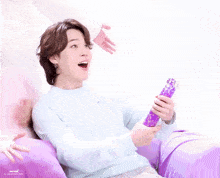 a person sitting on a purple couch holding a purple object with a surprised look on his face