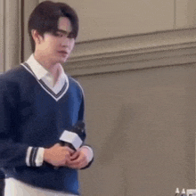 a young man in a blue sweater is holding a microphone while standing in front of a wall .
