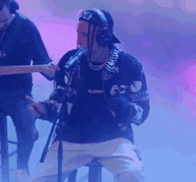 a man wearing headphones is singing into a microphone while another man plays a guitar in the background
