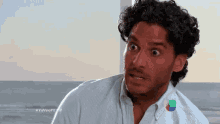 a man with curly hair is making a funny face while standing in front of the ocean .