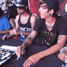 a man wearing a tank top that says cancer on it sits at a table