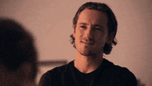 a man with long hair and a beard is smiling while looking at another man .