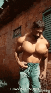a shirtless man with huge muscles is standing in front of a building .