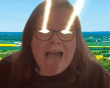 a woman wearing glasses is sticking her tongue out in front of a landscape