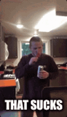 a man is standing in a kitchen holding a can of soda and eating a candy bar ..
