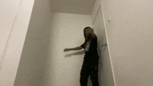 a man in a black shirt and black pants is standing next to a door in a room .