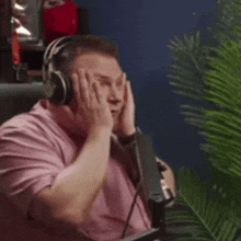 a man wearing headphones and a pink shirt is sitting in front of a microphone with his hands on his face .