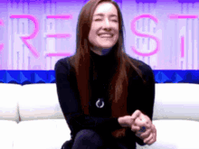 a woman sits on a white couch in front of a crest sign