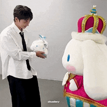 a man is standing next to a stuffed bunny wearing a crown and holding a stuffed animal .