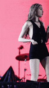 a woman in a black dress is standing on a stage in front of a drum set