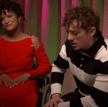 a woman in a red dress sits next to a man in a black and white striped sweater