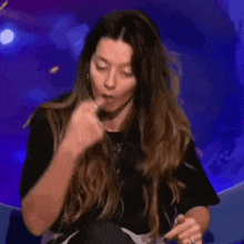 a woman with long hair is eating something with her fingers .