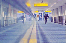 a blurred image of people walking in a hallway with a yellow sign that says ' exit ' on it