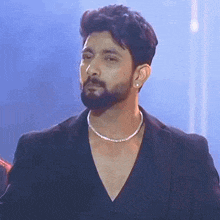 a man with a beard and a necklace is wearing a black suit .