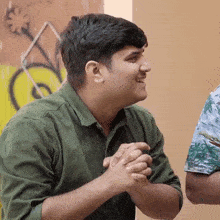 a man in a green shirt is smiling and holding his hands together