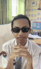 a young man wearing sunglasses and a tie looks at the camera with his hands folded